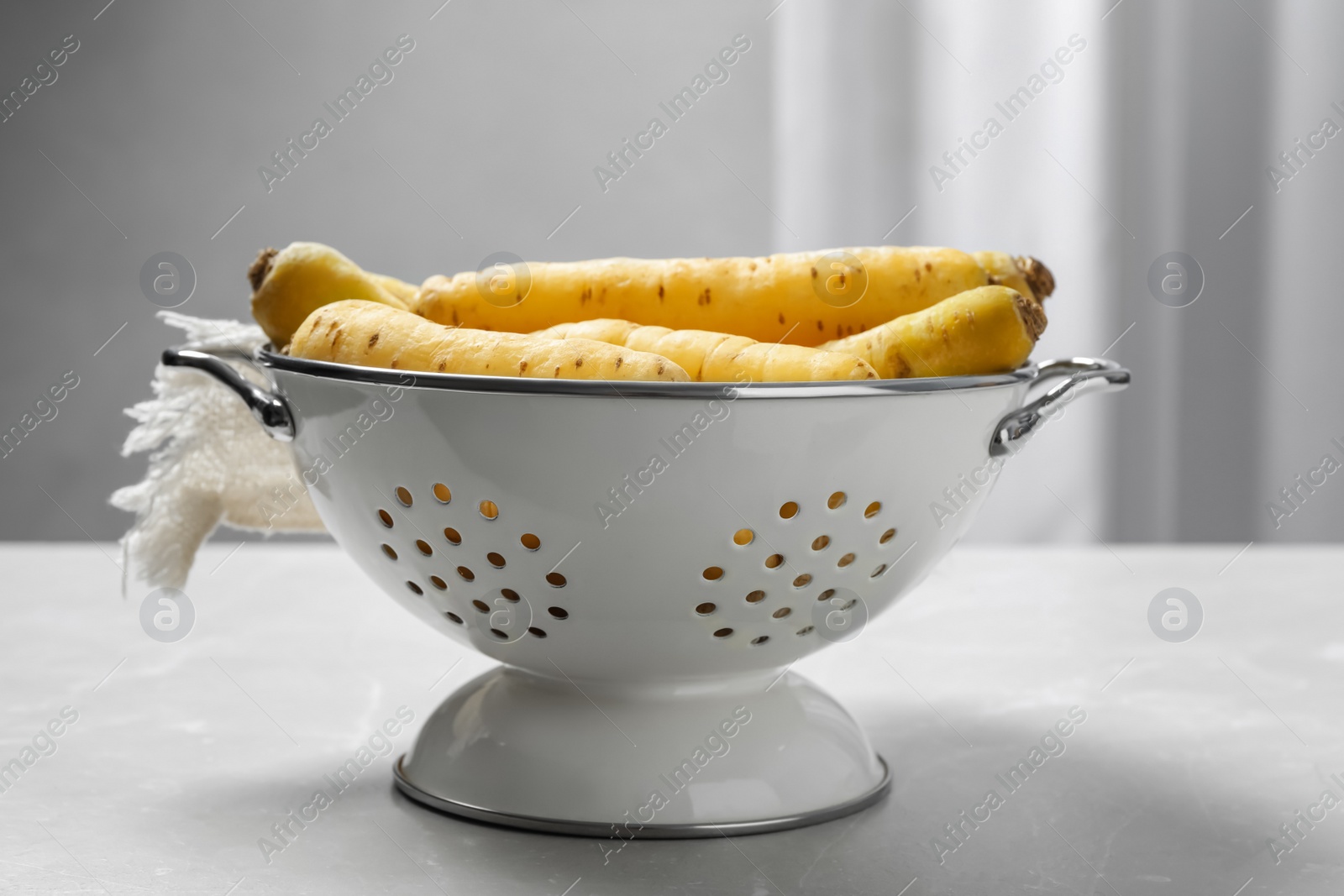 Photo of Raw white carrots in colander on light grey table