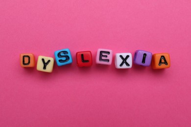 Colorful beads with word Dyslexia on pink background, flat lay