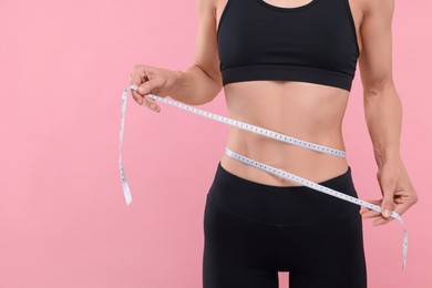 Photo of Slim woman measuring waist with tape on pink background, closeup and space for text. Weight loss