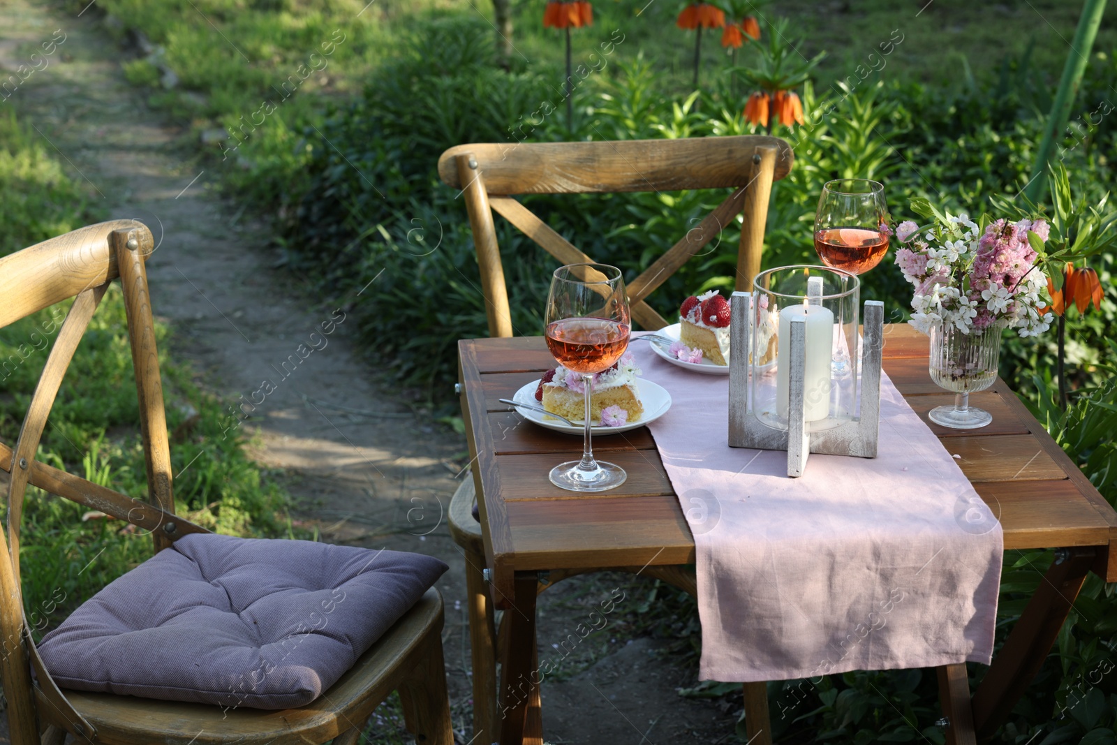 Photo of Vase with spring flowers, wine and cake on table served for romantic date in garden