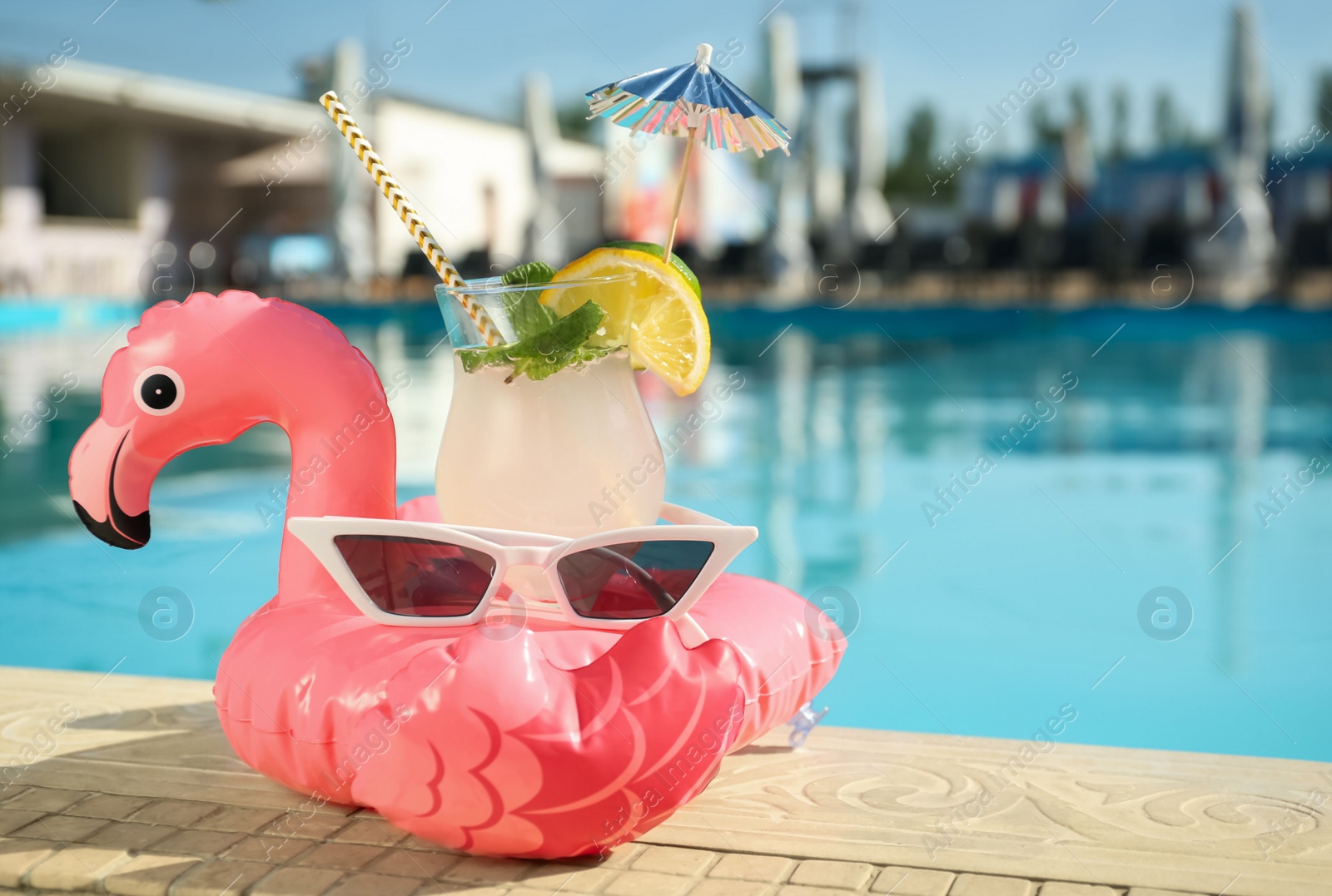 Photo of Tasty refreshing cocktail and sunglasses on edge of swimming pool. Party items