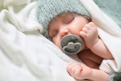Cute newborn baby with pacifier sleeping on white blanket, closeup