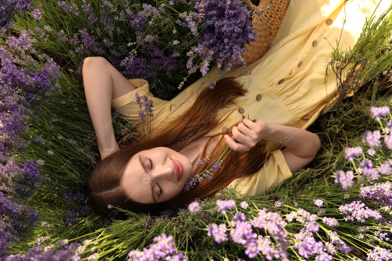 Photo of Young woman lying in lavender field on summer day, top view