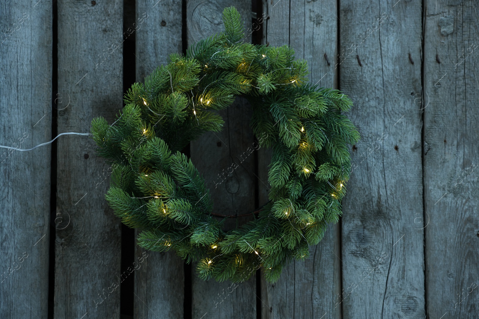 Photo of Beautiful Christmas wreath with string lights hanging on wooden wall