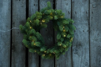 Beautiful Christmas wreath with string lights hanging on wooden wall