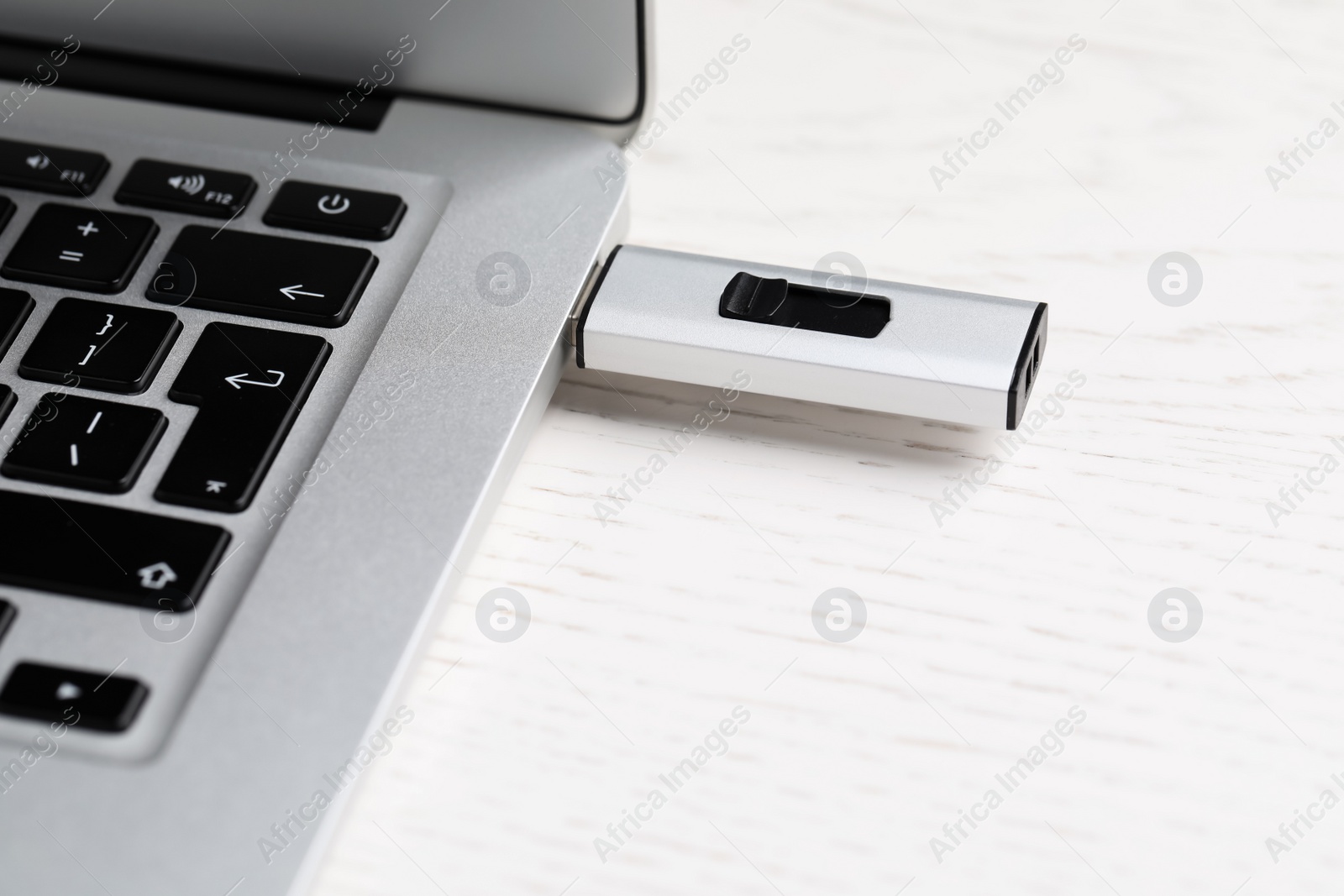 Photo of Modern usb flash drive attached into laptop on white wooden table, closeup