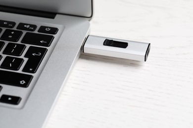 Modern usb flash drive attached into laptop on white wooden table, closeup