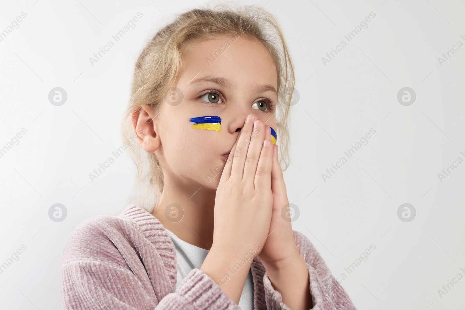 Photo of Little girl with drawings of Ukrainian flag on face and clasped hands against white background