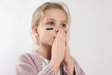 Photo of Little girl with drawings of Ukrainian flag on face and clasped hands against white background