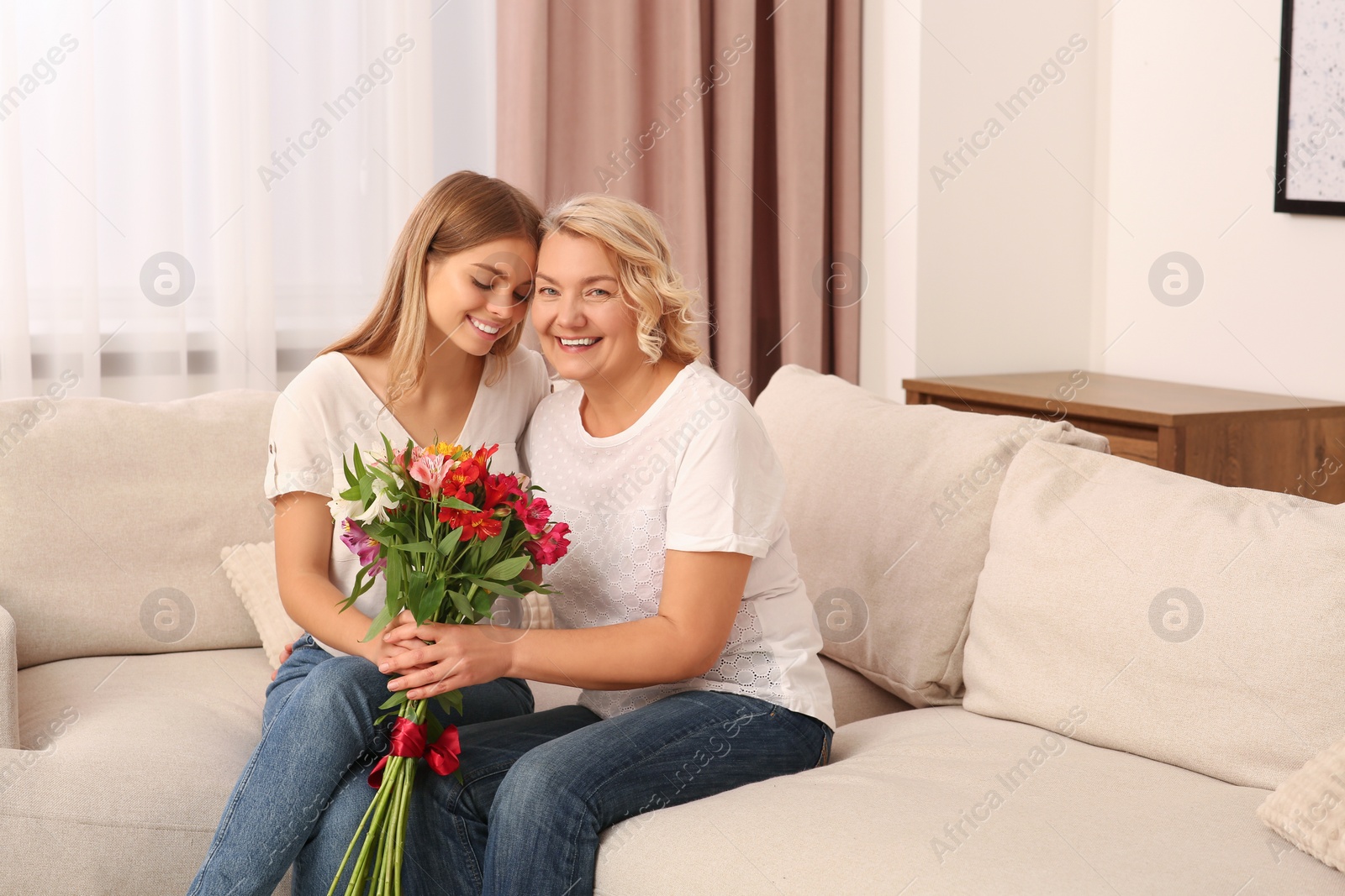 Photo of Young daughter congratulating her mom with flowers at home. Happy Mother's Day