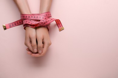 Woman tied with measuring tape on pink background, top view and space for text. Diet concept