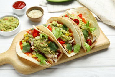 Delicious tacos with guacamole, meat and vegetables served on white wooden table, closeup