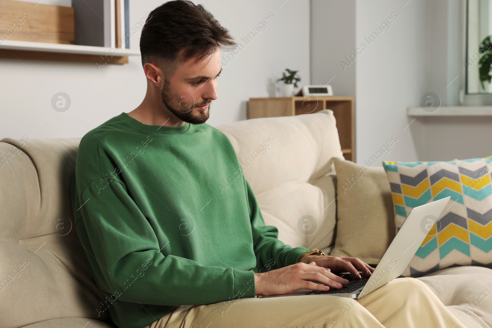 Photo of Handsome man with laptop sitting on sofa at home