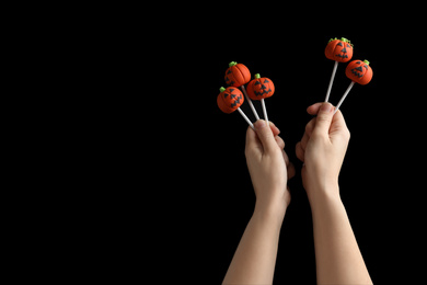 Woman with delicious pumpkin shaped cake pops and space for text on black background, closeup. Halloween celebration