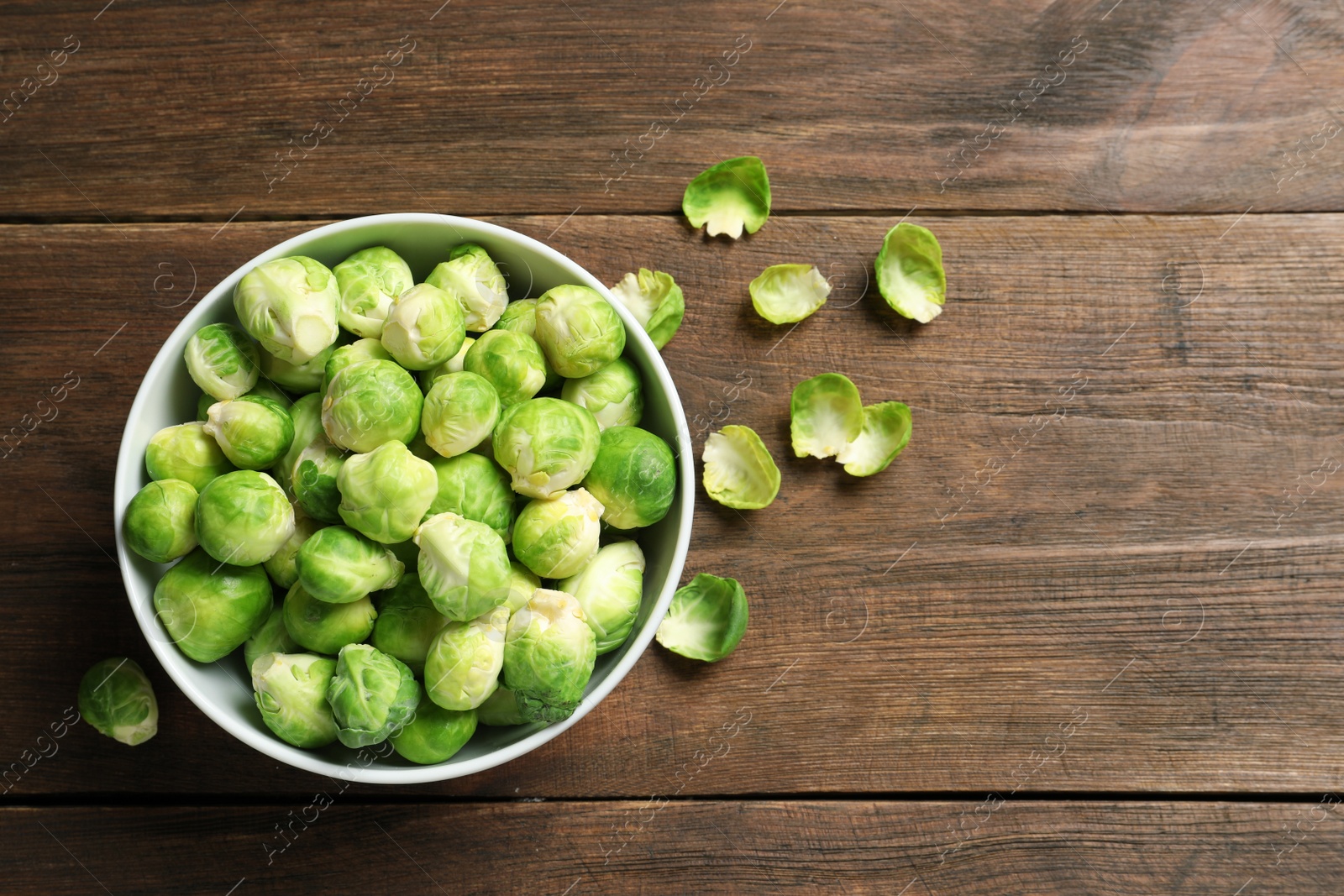 Photo of Bowl of fresh Brussels sprouts and leaves on wooden background, top view with space for text