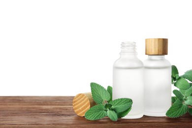 Bottles of essential oil and mint on wooden table against white background