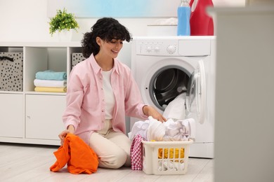 Photo of Happy woman with laundry near washing machine indoors