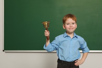 Photo of Pupil with school bell near green chalkboard in classroom