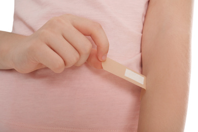 Photo of Preteen girl putting sticking plaster onto arm on white background, closeup