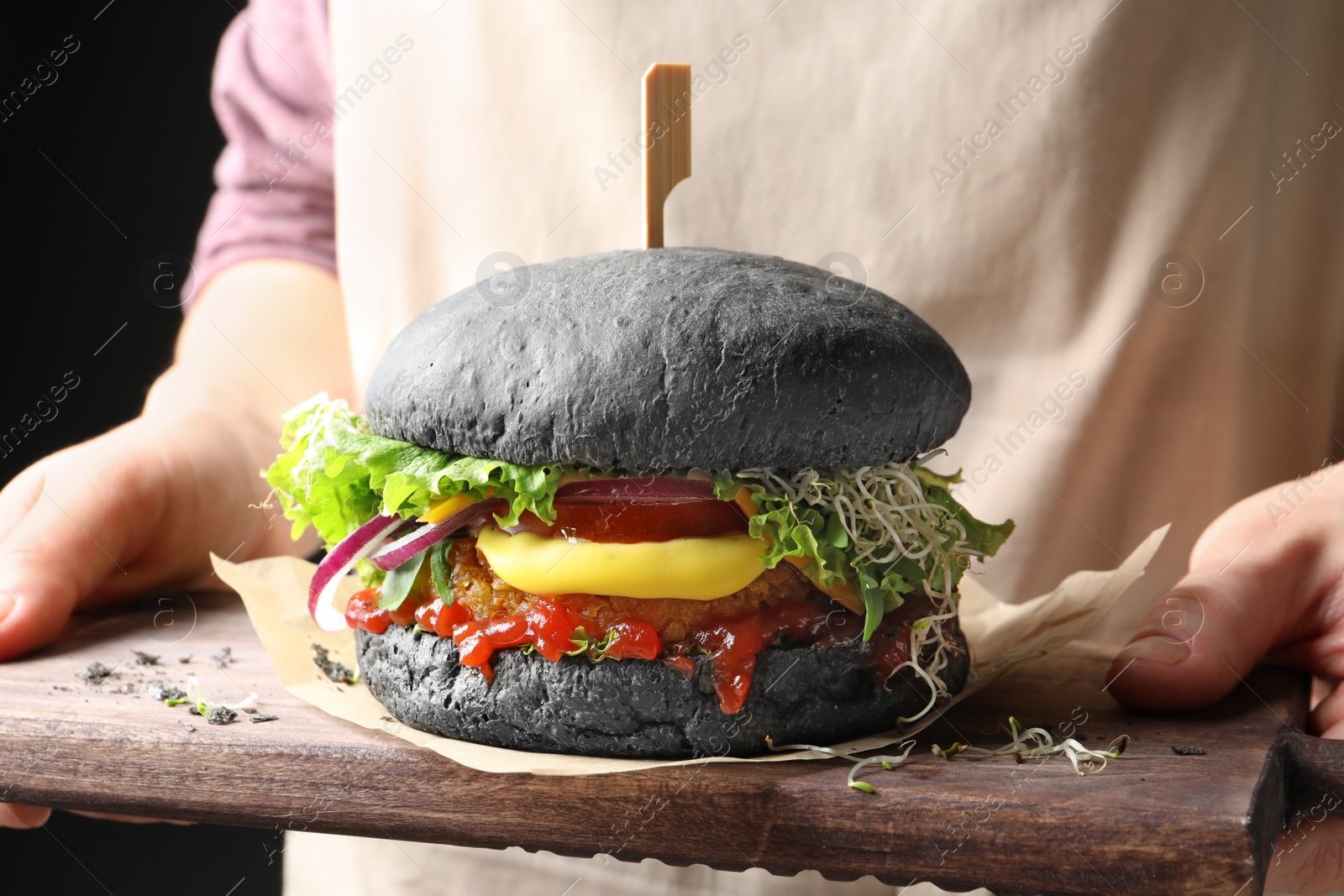 Photo of Woman holding board with tasty black vegetarian burger, closeup