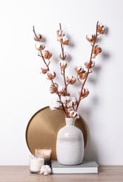 Photo of Candles, book and vase with cotton branches on wooden table against white background