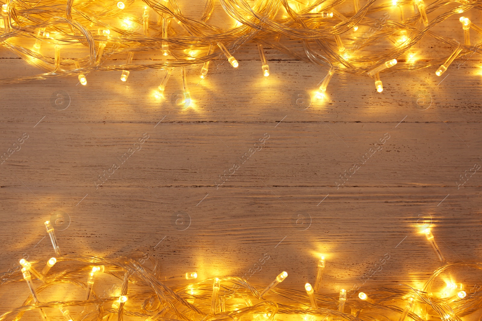 Photo of Glowing Christmas lights on white wooden background, top view. Space for text