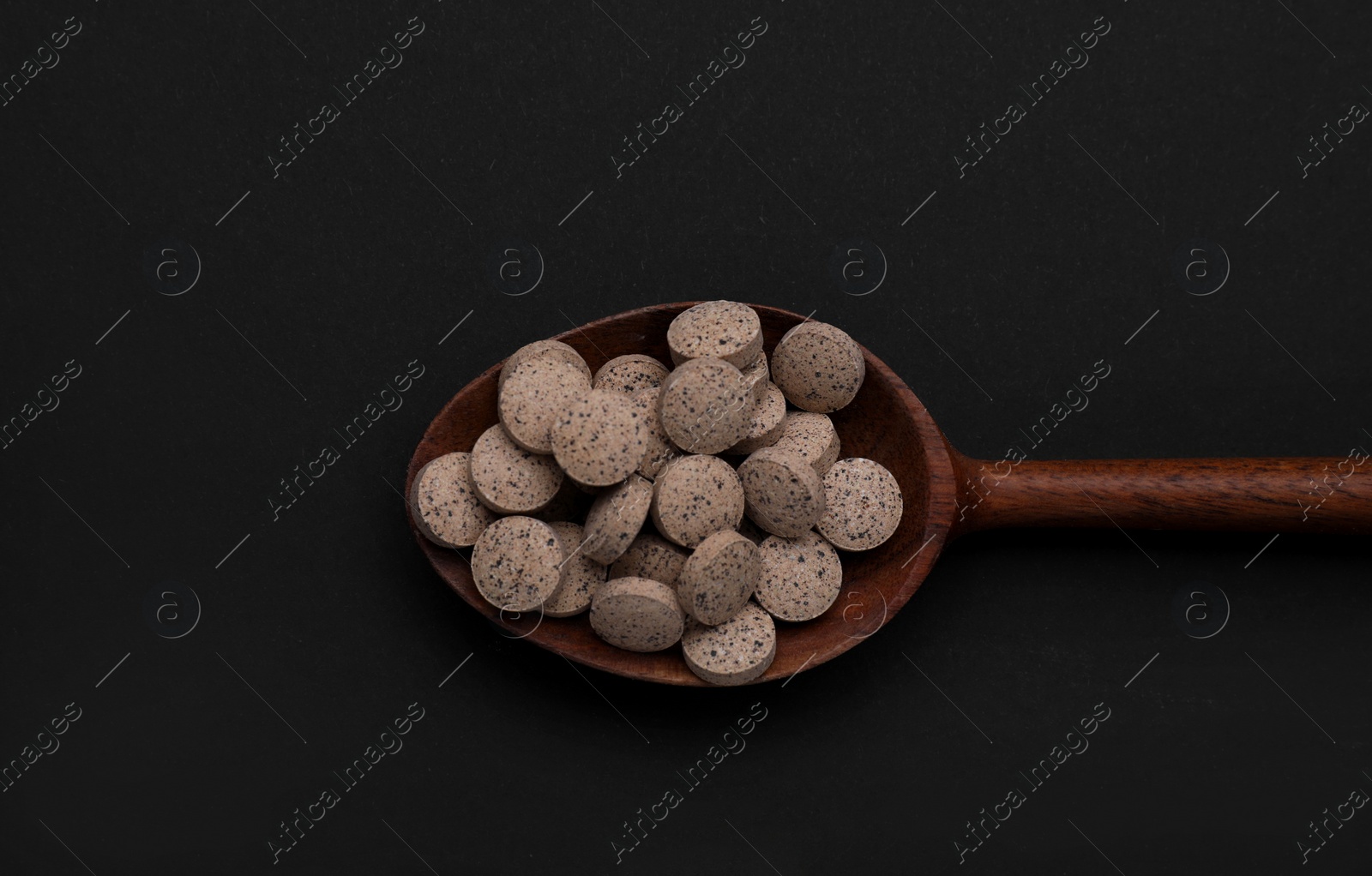 Photo of Wooden spoon of brewer`s yeast tablets on black background, top view