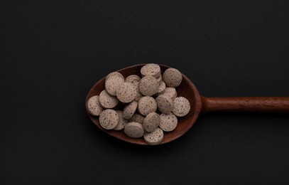 Photo of Wooden spoon of brewer`s yeast tablets on black background, top view