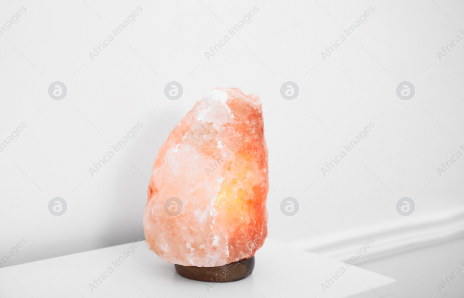 Photo of Himalayan salt lamp on console table near white wall. Space for text