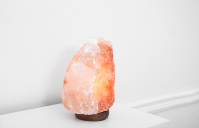 Photo of Himalayan salt lamp on console table near white wall. Space for text