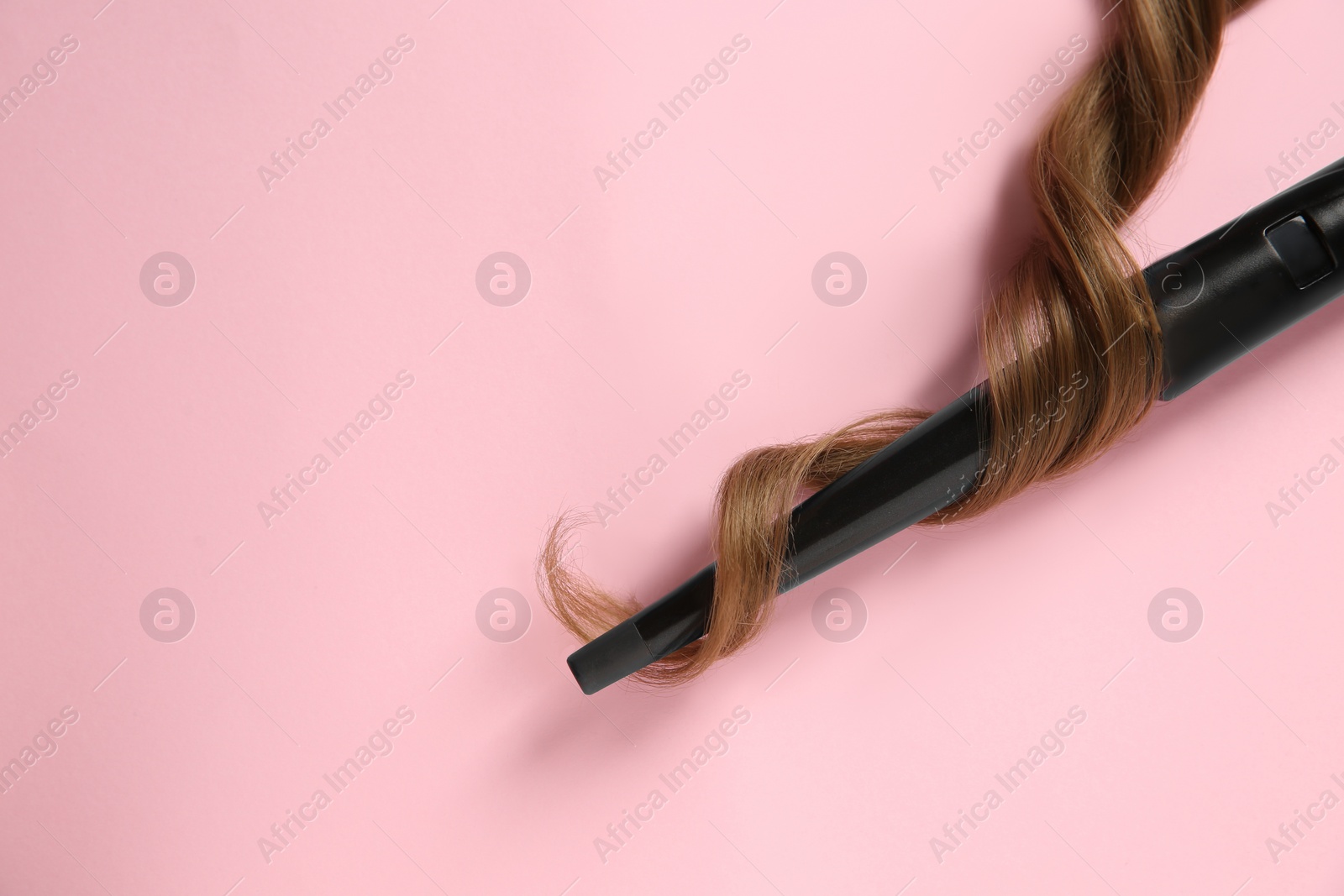 Photo of Modern clipless curling iron and brown hair lock on pink background, top view. Space for text