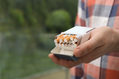 Photo of Man holding pack with cigarettes on blurred background, closeup. Space for text