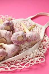 Photo of String bag with garlic heads on bright pink background, closeup