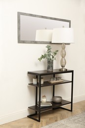 Modern console table with stylish decor and mirror on white wall in room. Interior design