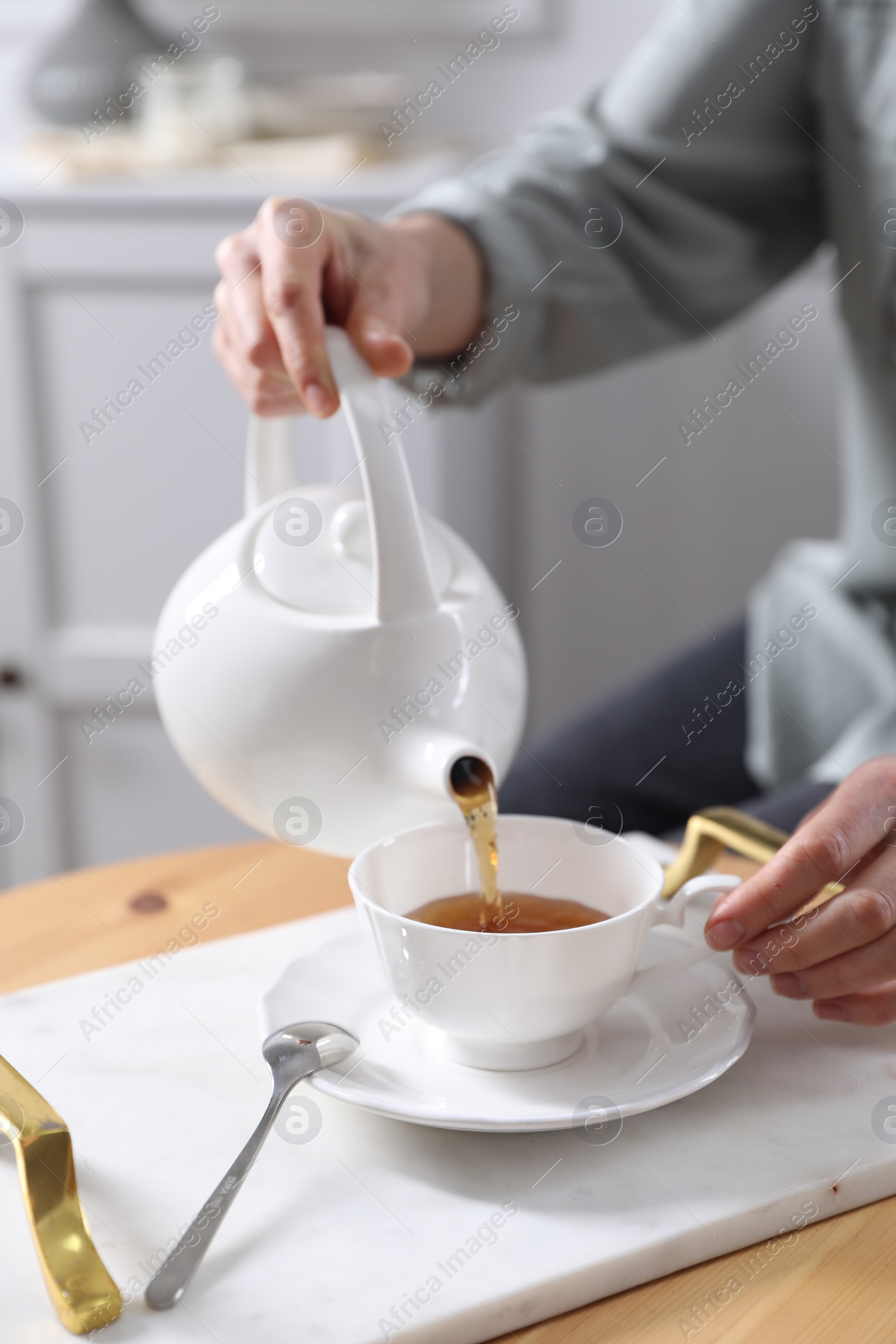 Photo of Woman pouring hot tea into cup at wooden table, closeup