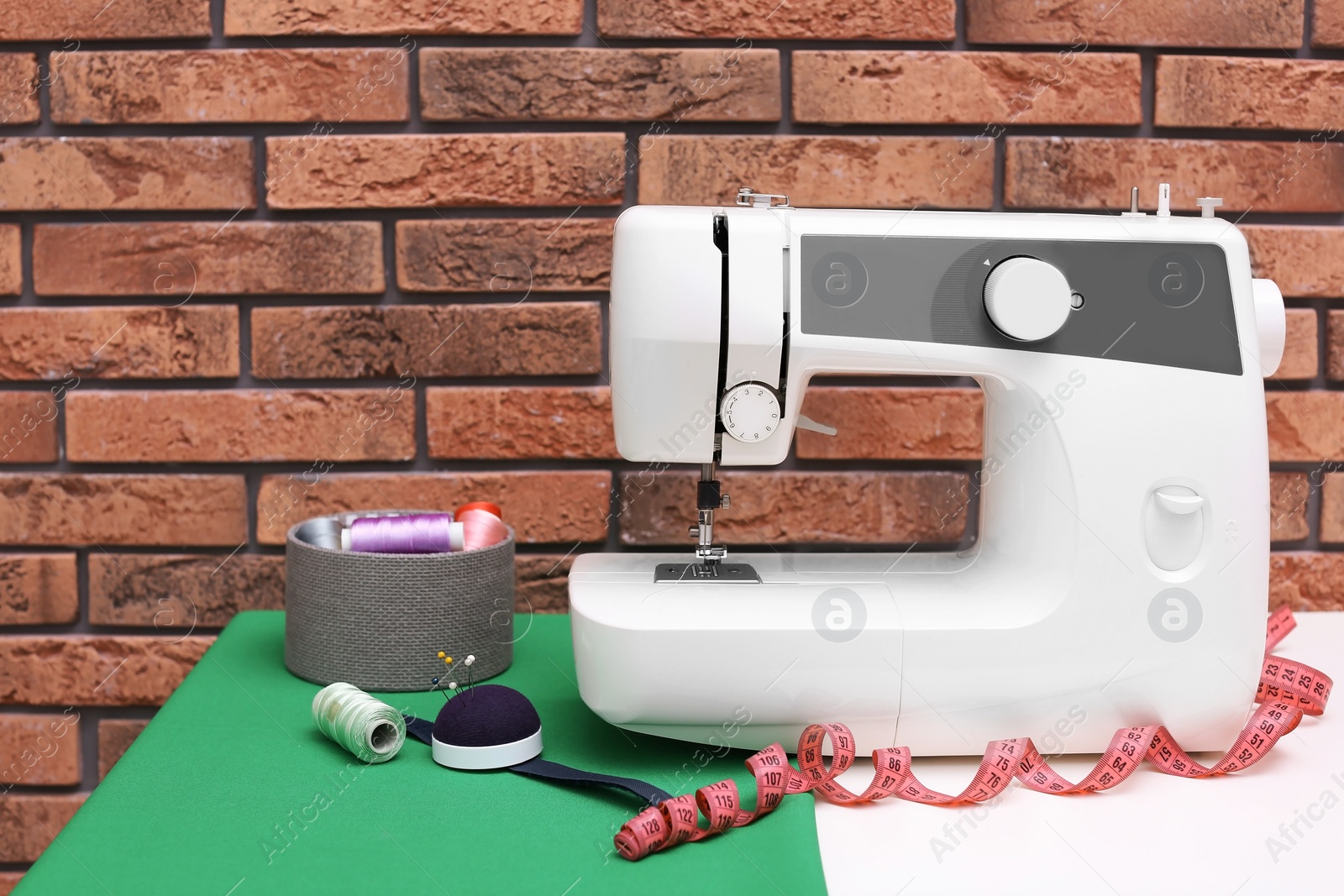 Photo of Modern sewing machine on table near brick wall