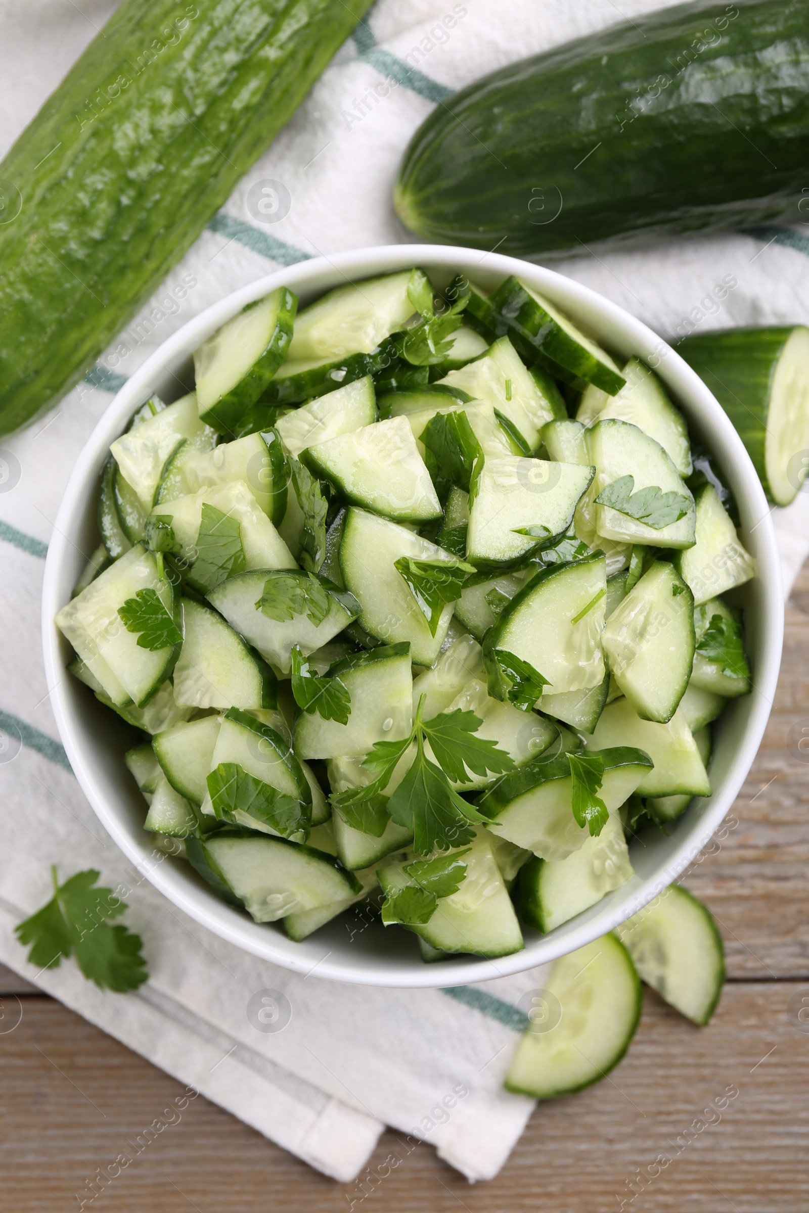 Photo of Delicious cucumber salad in bowl on wooden table, flat lay