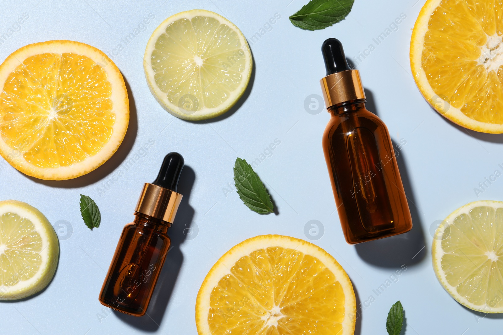 Photo of Bottles of cosmetic serum, sliced citrus fruits and green leaves on light blue background, flat lay