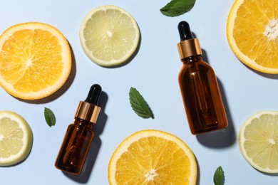 Bottles of cosmetic serum, sliced citrus fruits and green leaves on light blue background, flat lay