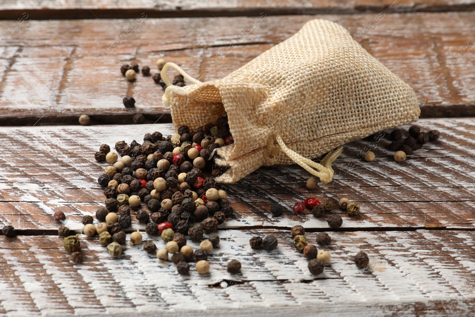 Photo of Aromatic spice. Different peppers in burlap bag on wooden table