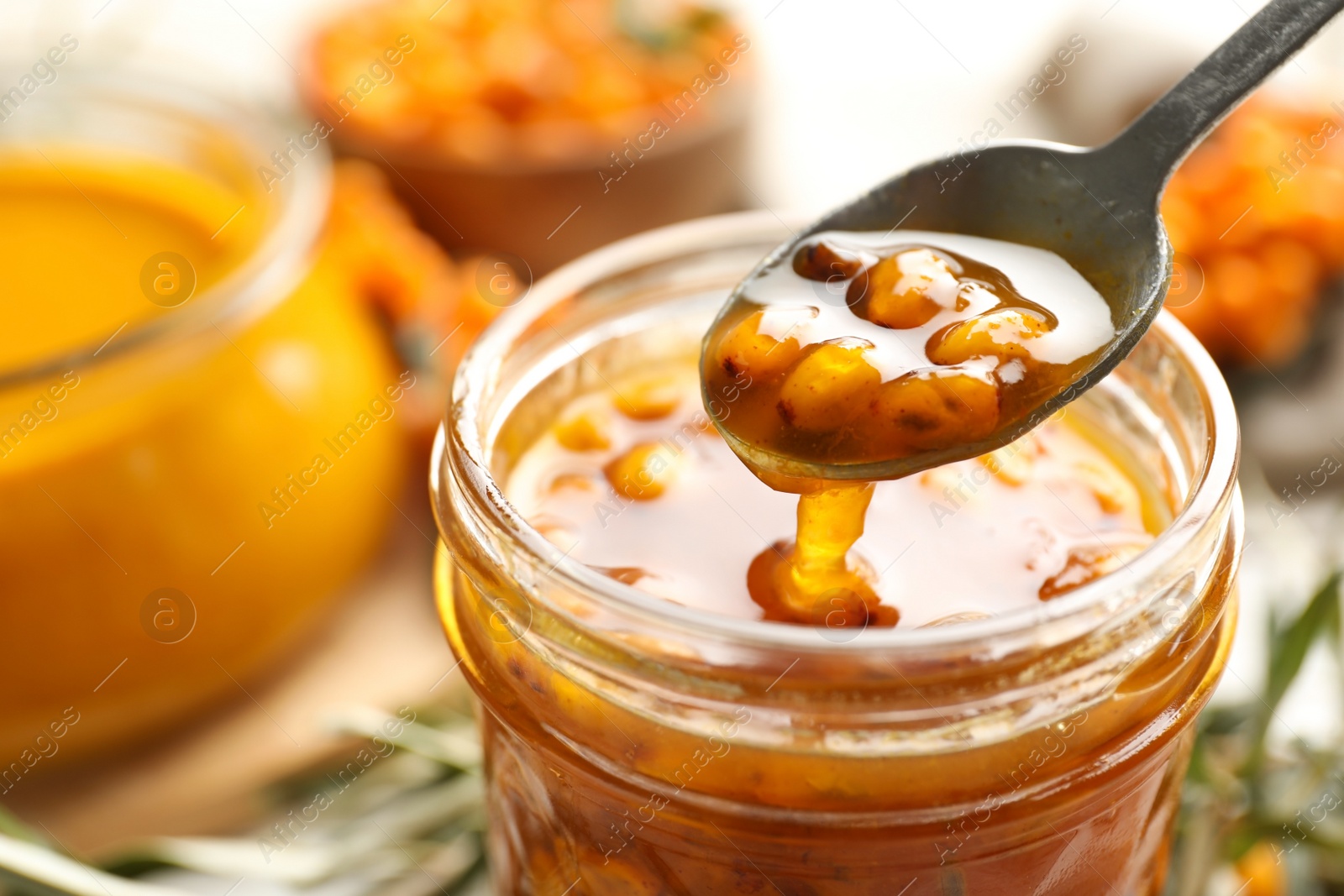 Photo of Spoon with delicious sea buckthorn jam over jar, closeup