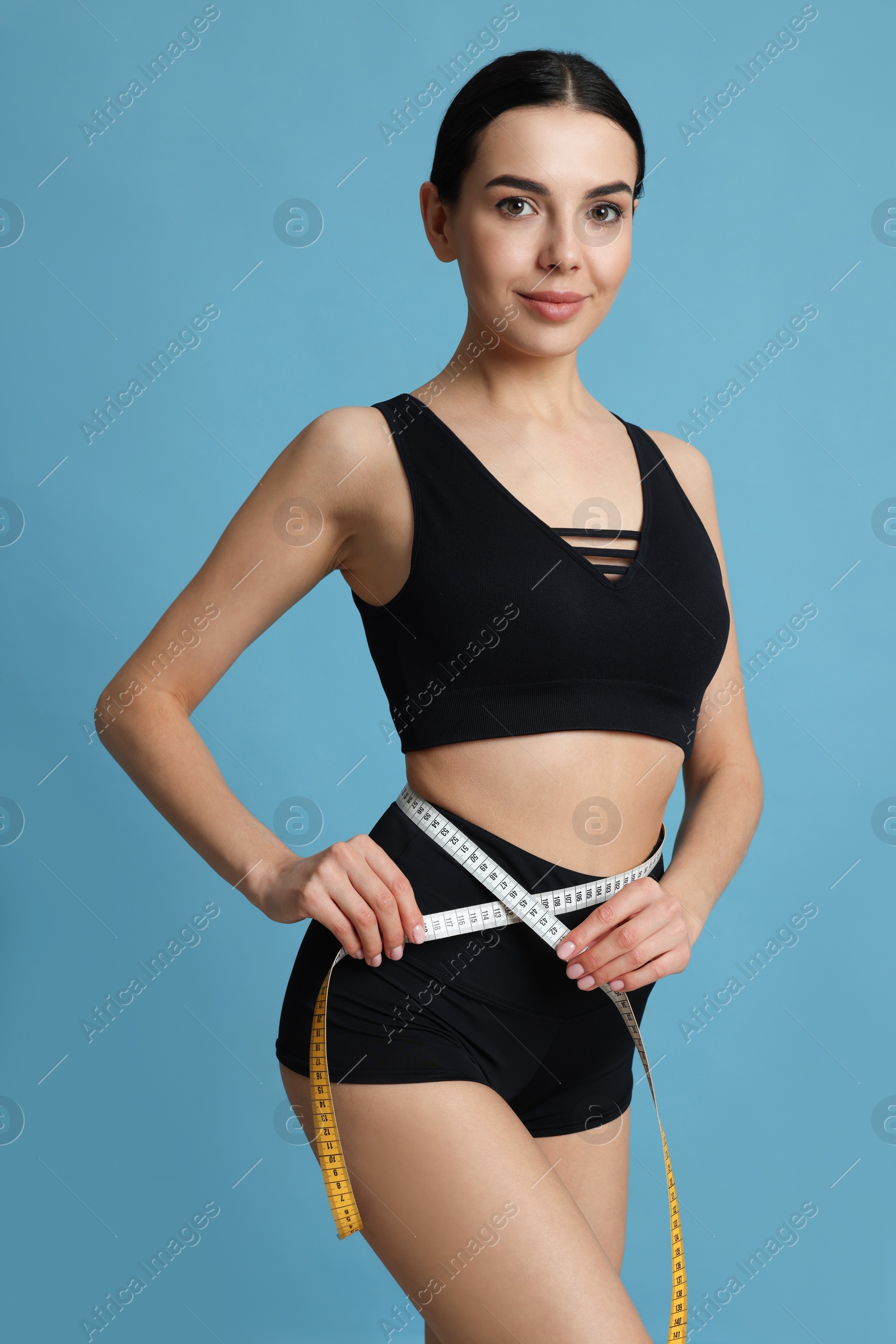 Photo of Young woman measuring waist with tape on light blue background