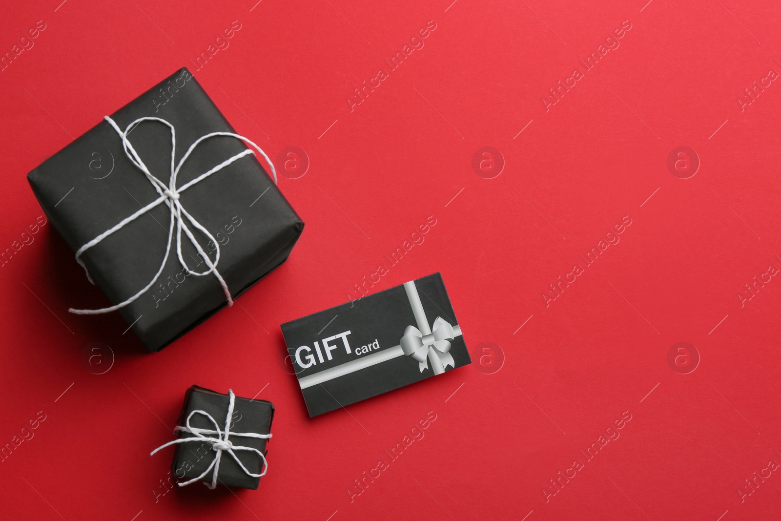 Photo of Gift card and presents on red background, flat lay. Space for text