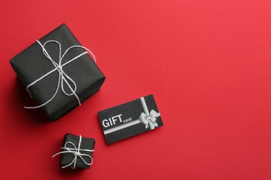 Photo of Gift card and presents on red background, flat lay. Space for text