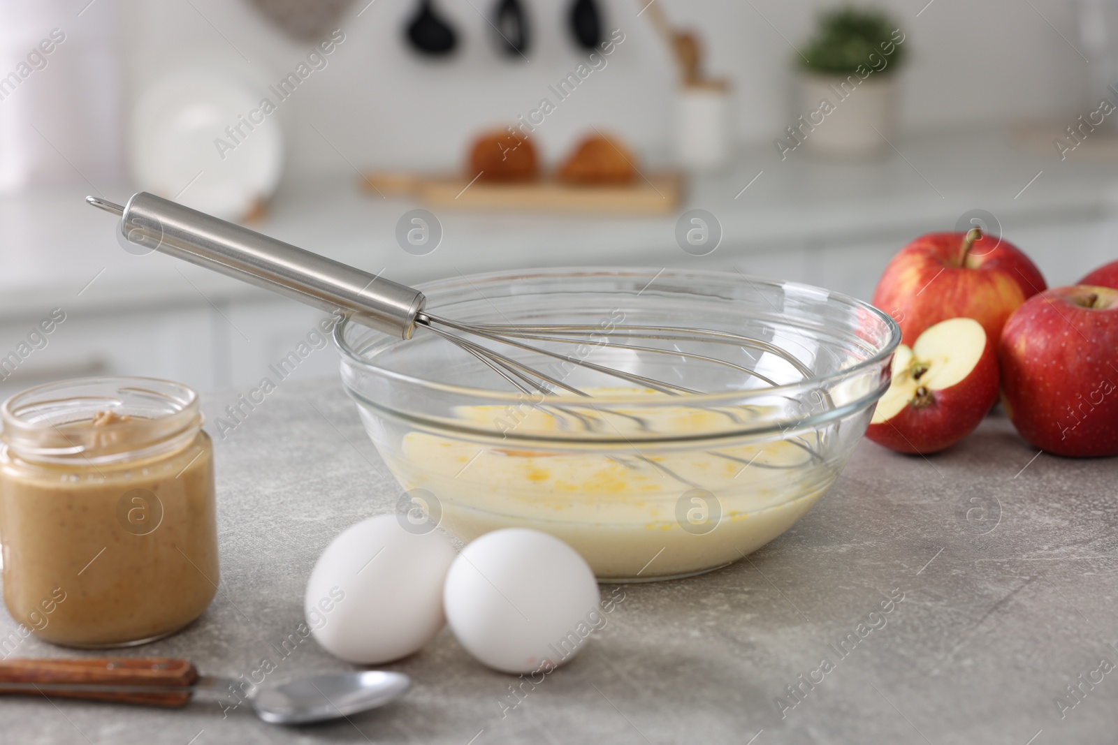 Photo of Whisk, bowl, beaten eggs and other ingredients on grey table indoors