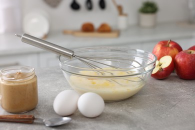 Whisk, bowl, beaten eggs and other ingredients on grey table indoors