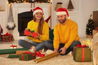 Photo of Happy couple in Santa hats decorating Christmas gifts at home