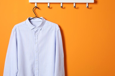 Photo of Hanger with striped shirt on orange wall, space for text
