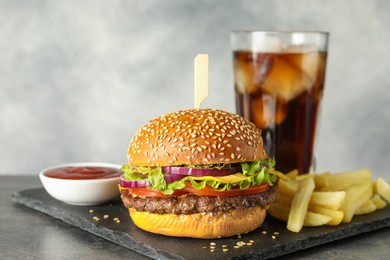 Photo of Burger with delicious patty, soda drink, french fries and sauce on dark table against gray background, closeup
