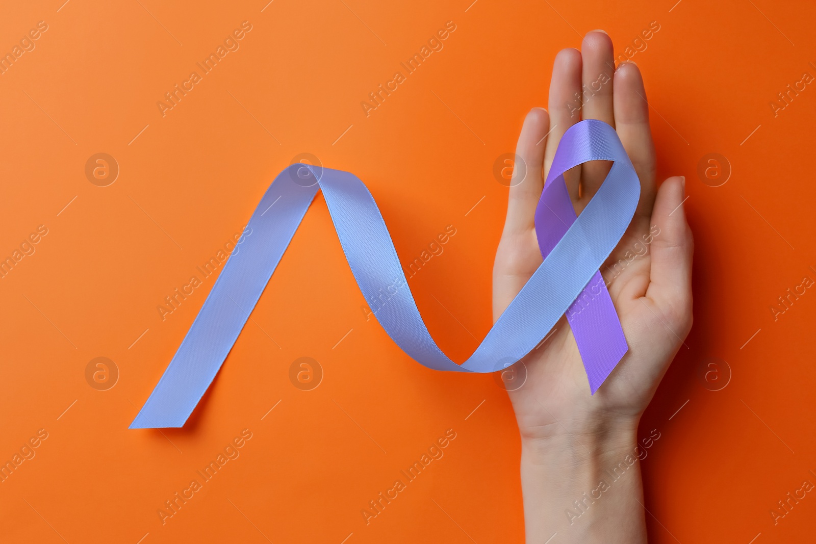 Image of World Arthritis Day. Woman with blue and purple awareness ribbon on orange background, top view